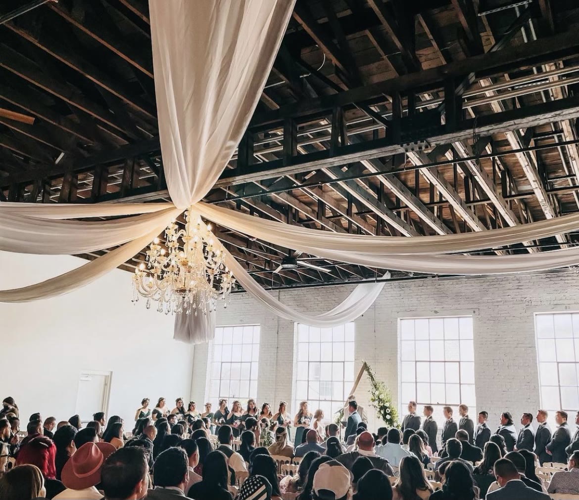 Ivory drapery sweeping from the ballroom chandelier out over a full congregation during a ceremony.