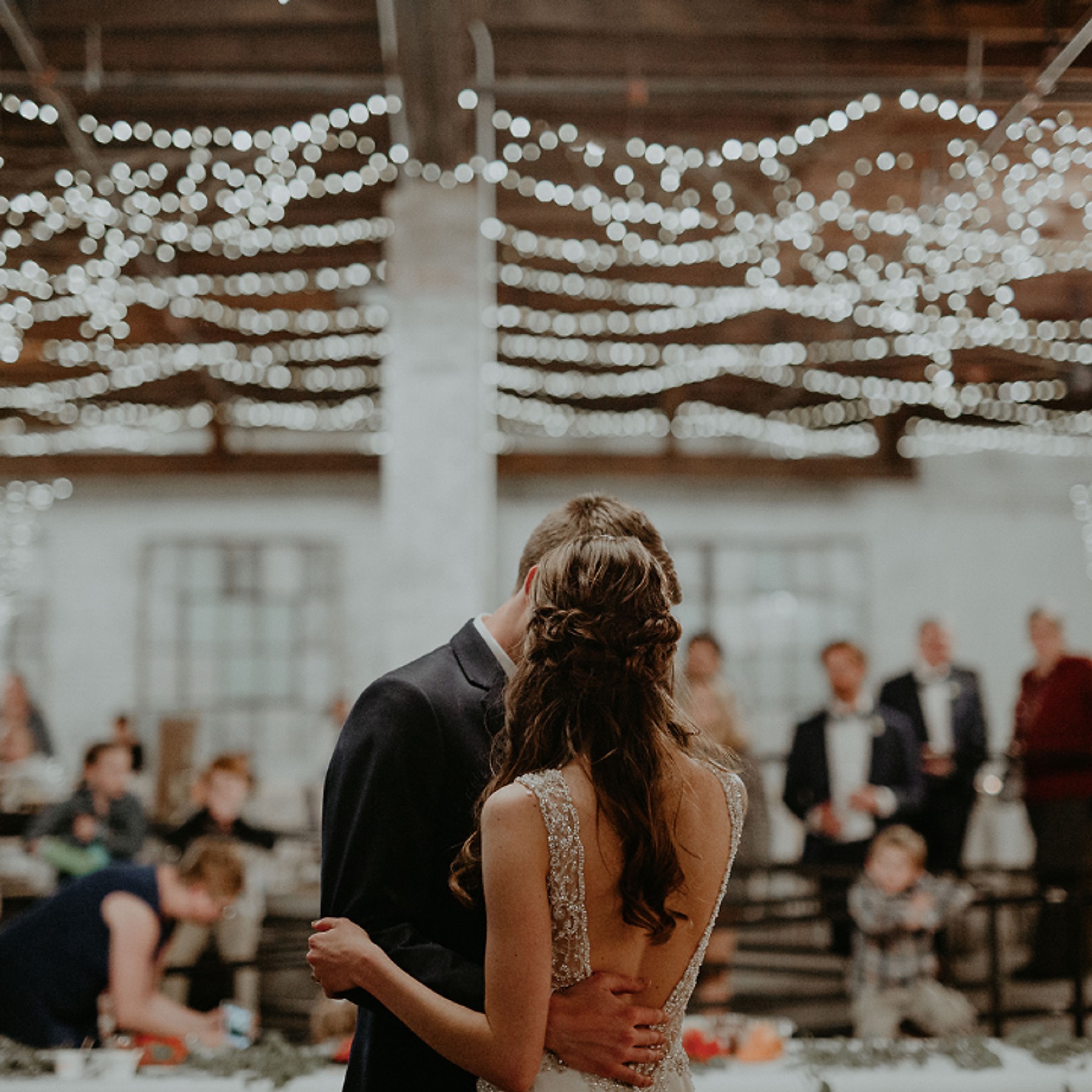 A first dance beneath strings of fairy lights in the main ballroom, guests looking on.