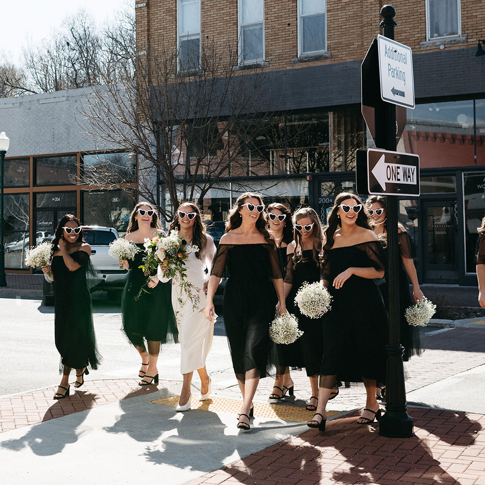 A bride and her bridal party walking through downtown Siloam Springs, past its historic brick storefronts.