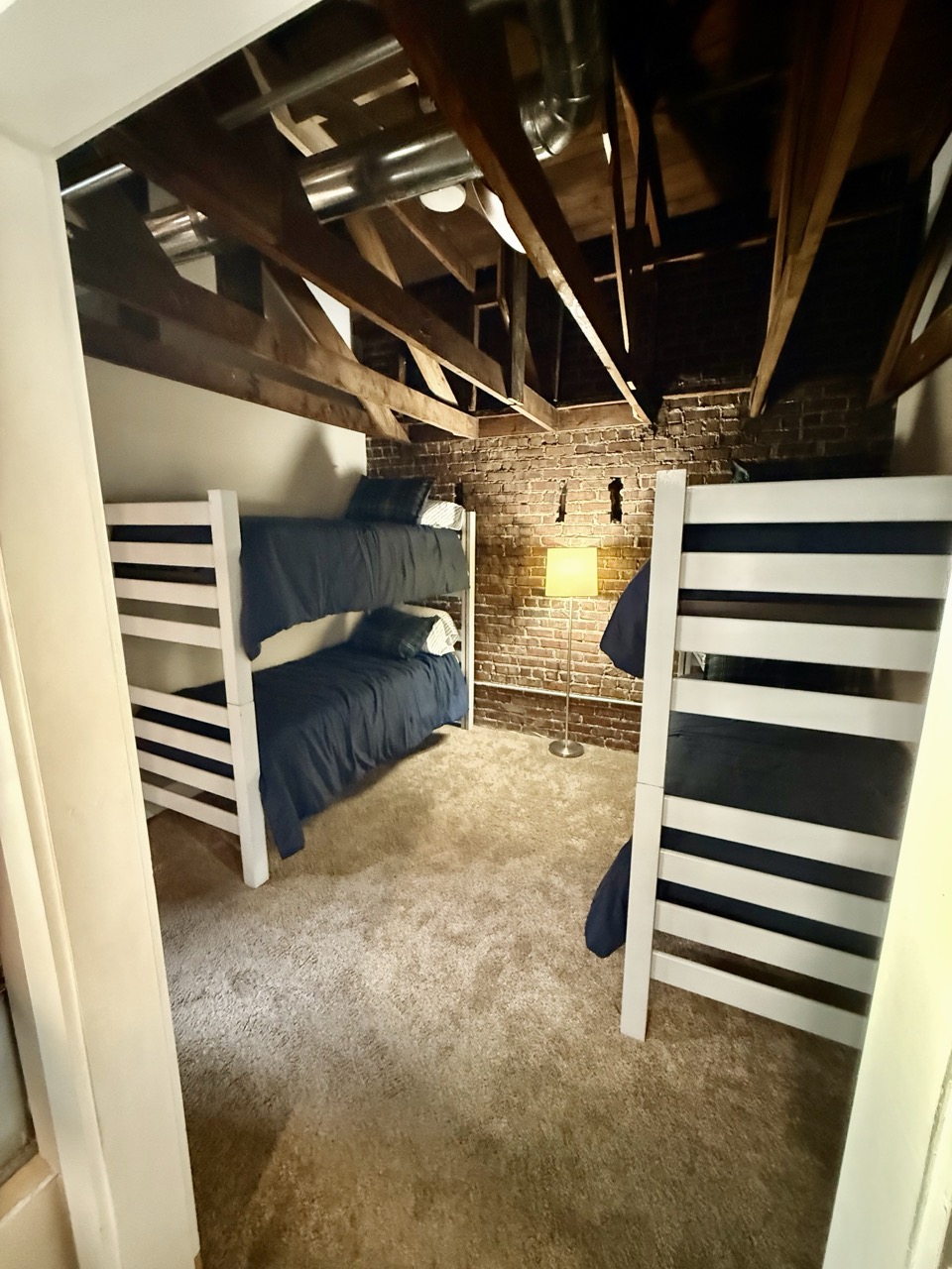 A bunk room with navy bedding, white bunk frames tucked under the sloping timber roof.