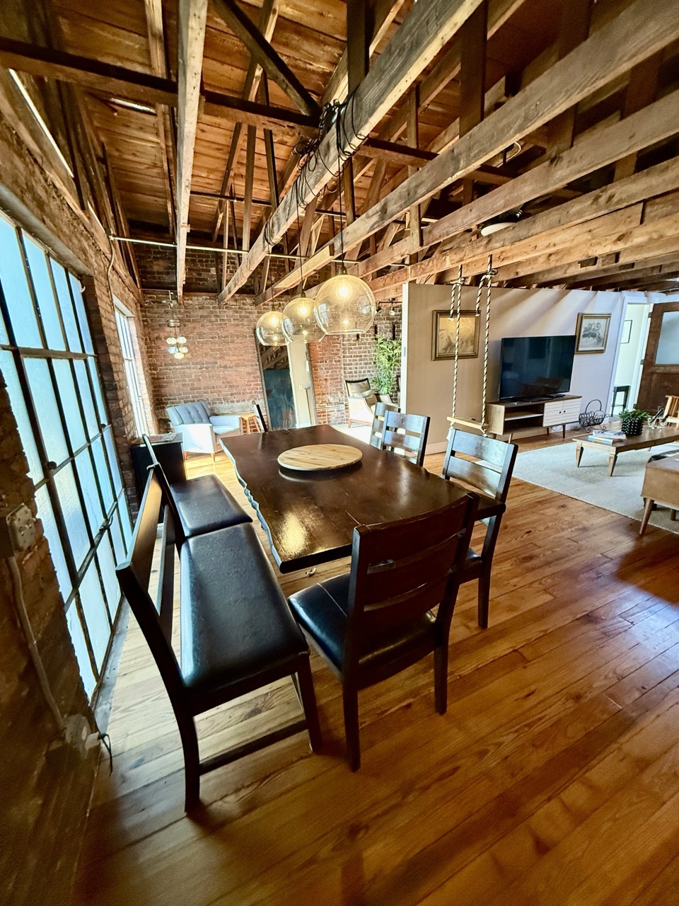 The dining table under hanging pendant globes, tall industrial windows to one side.