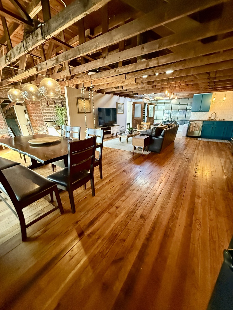The loft's dining and living area seen from the door, timber trusses overhead and wood floors running throughout.