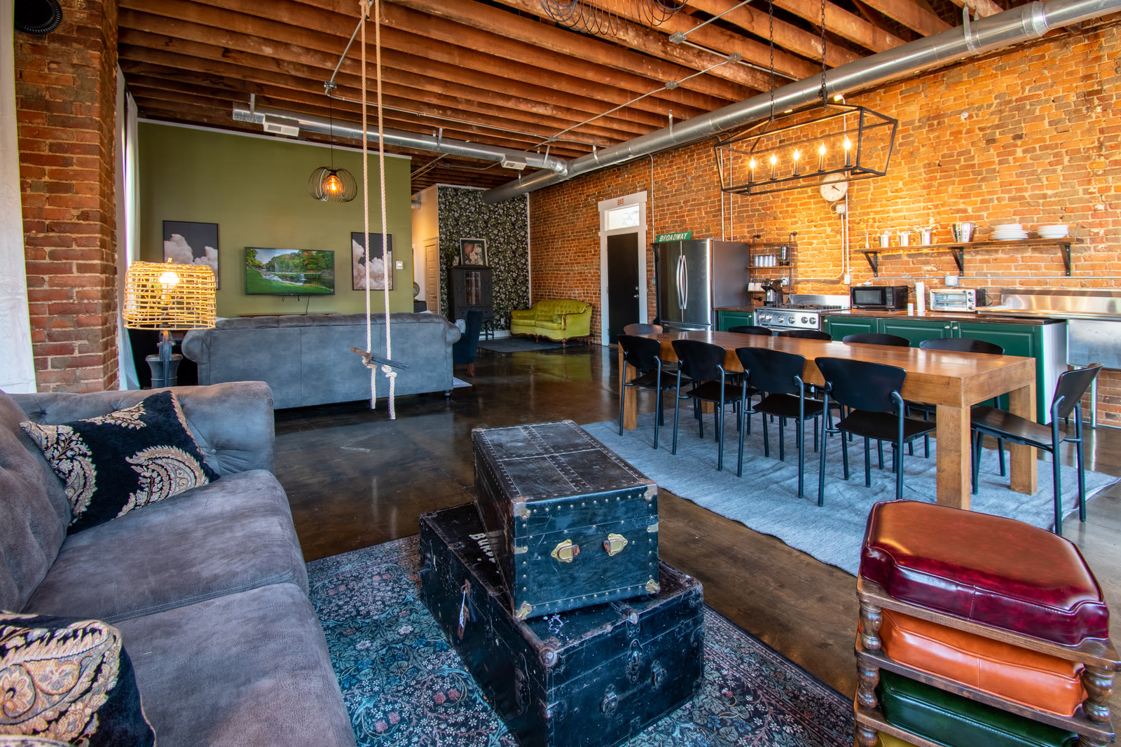 The Hidden Loft's living space: a hanging swing, a vintage steamer trunk and a long communal table under exposed brick and timber beams.