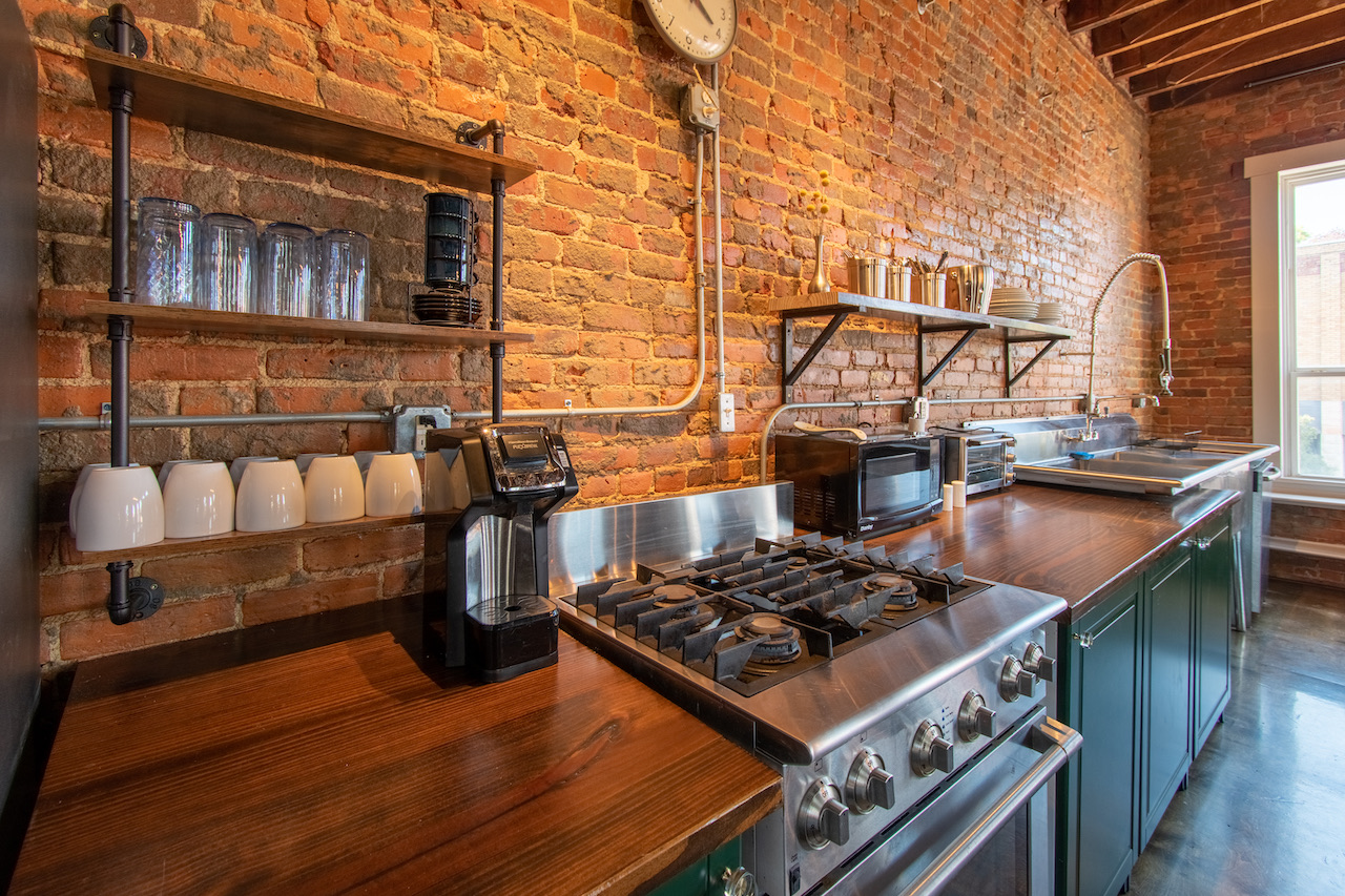 The kitchen: open shelves of glassware mounted on bare brick, a stainless gas range, and butcher-block counters.