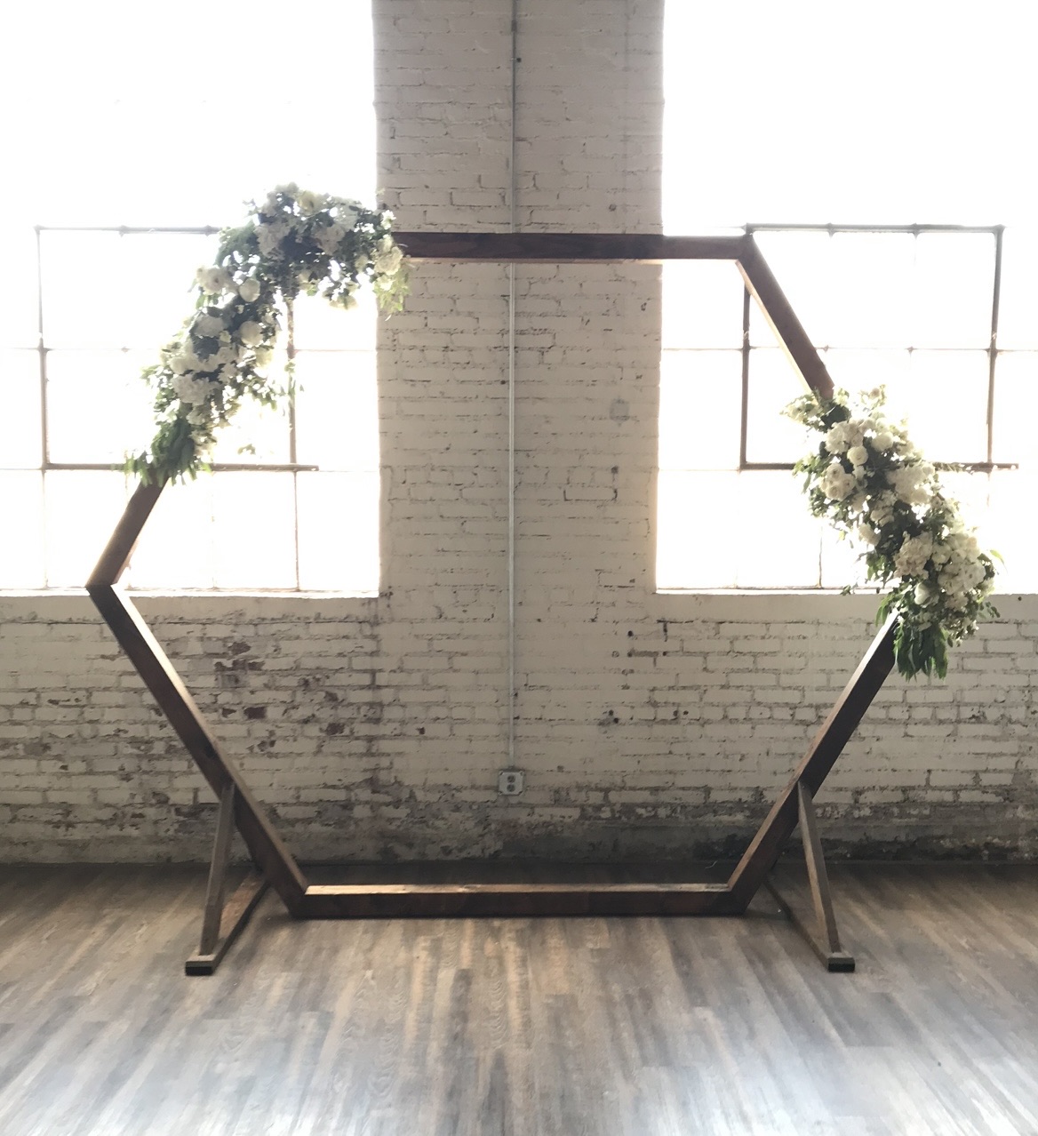 The hexagon arbor: a dark hexagonal frame against whitewashed brick, greenery gathered at two of its corners.