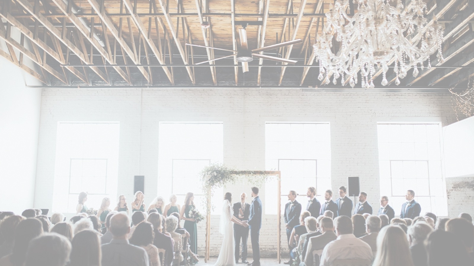 A wide black-and-white view of a ceremony in the ballroom, guests filling the room on both sides of the aisle.