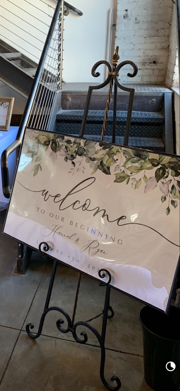 A black wrought-iron easel with scrolled legs, holding a printed welcome sign.