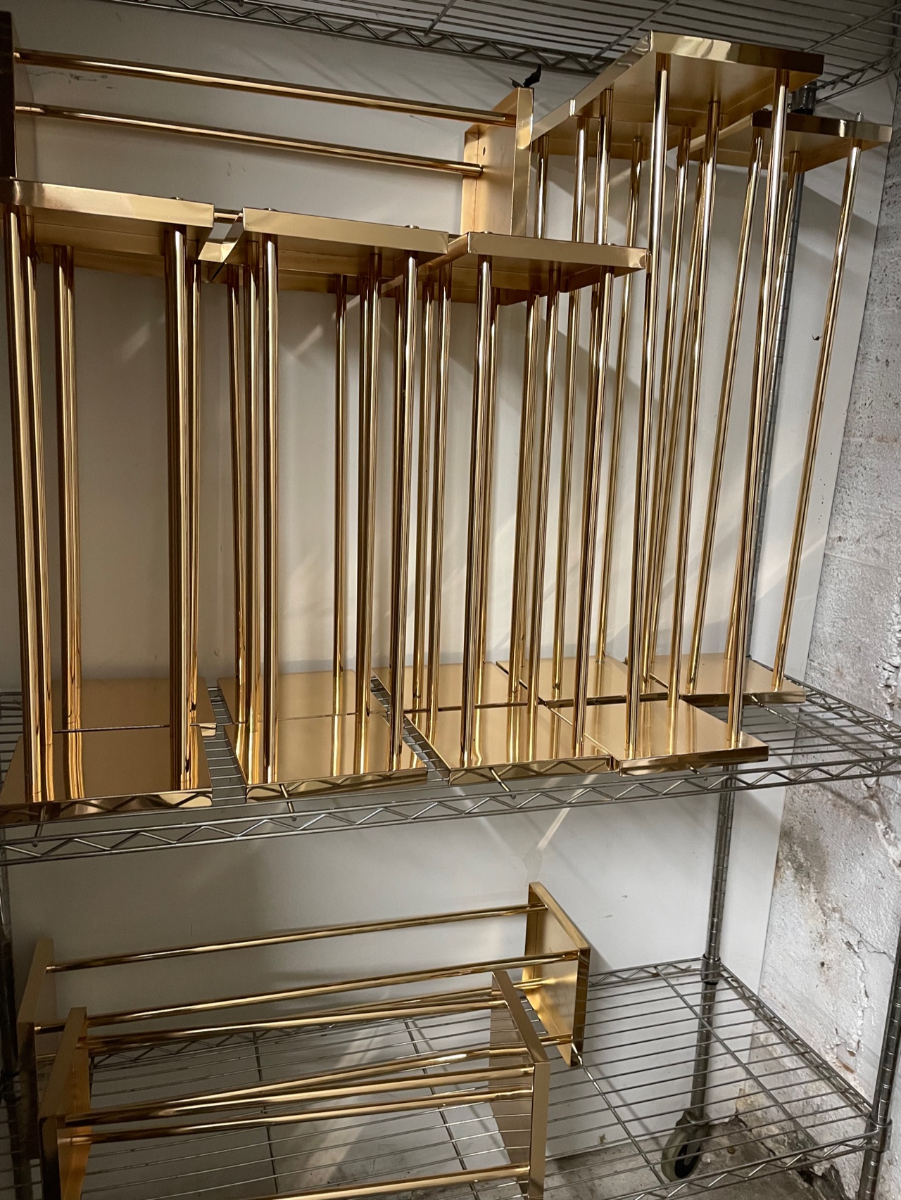 A stack of slim gold metal frames and stands resting on a wire storage rack.