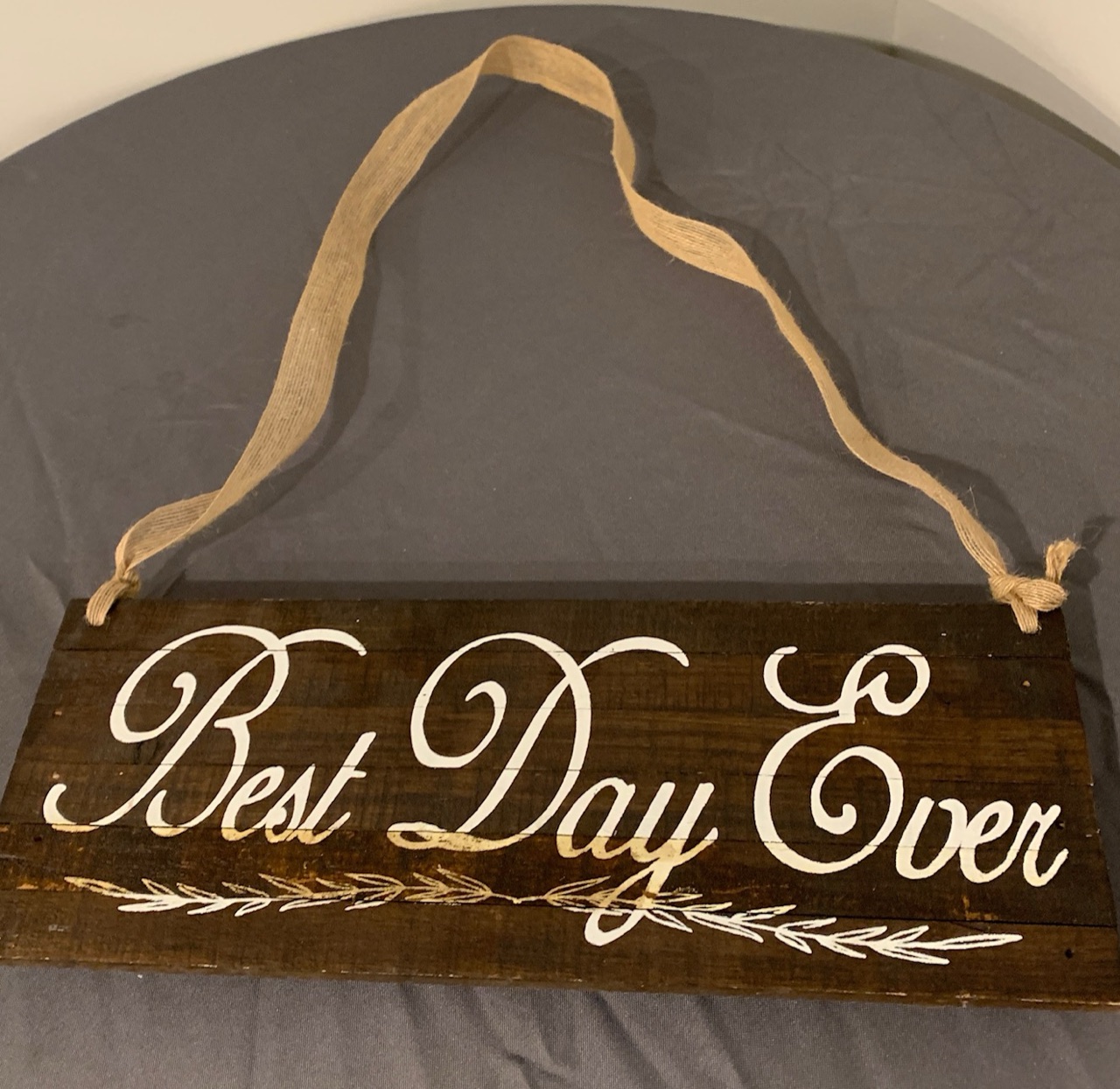A dark wooden sign painted with the words Best Day Ever in white script, hung from a burlap ribbon.