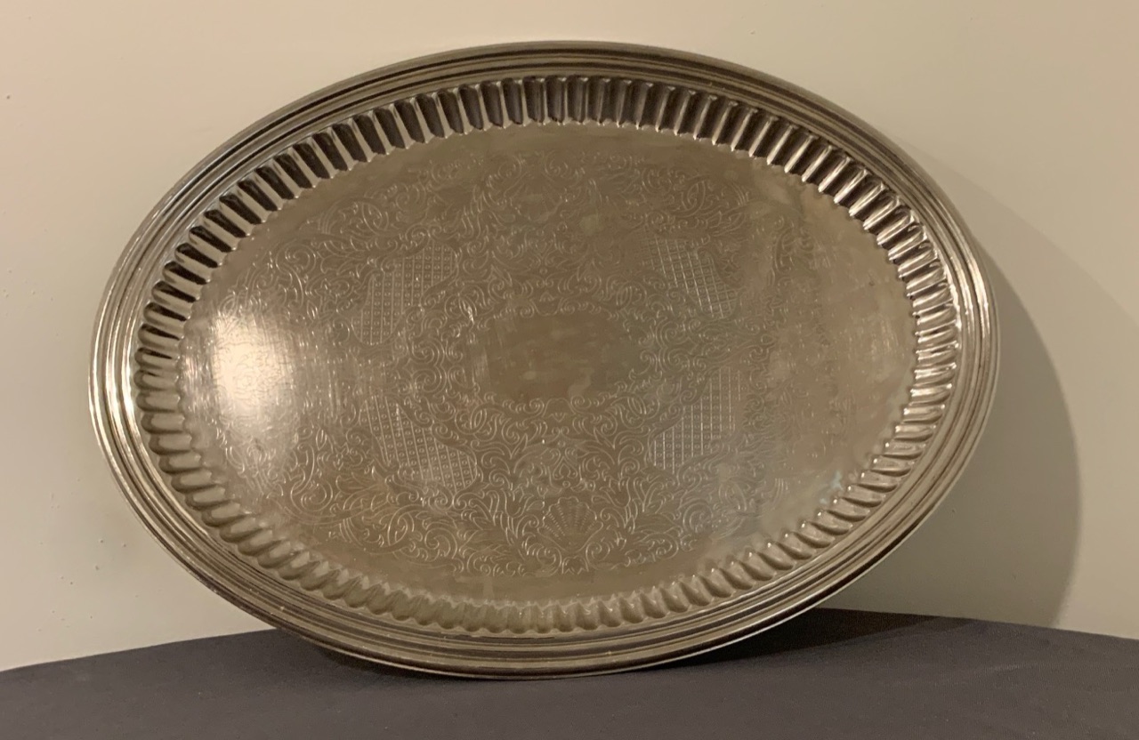 An oval silver serving tray with an etched centre and a fluted rim.