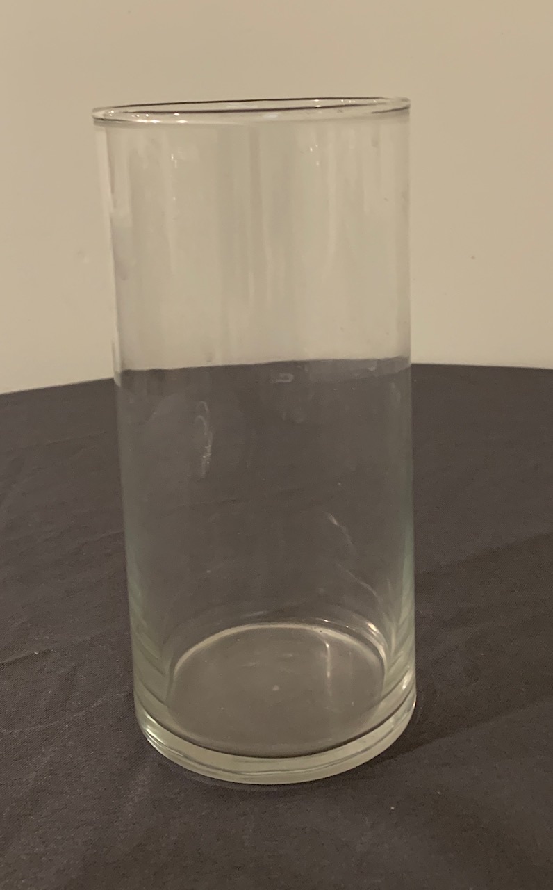 A tall straight-sided clear glass cylinder vase on a dark table.