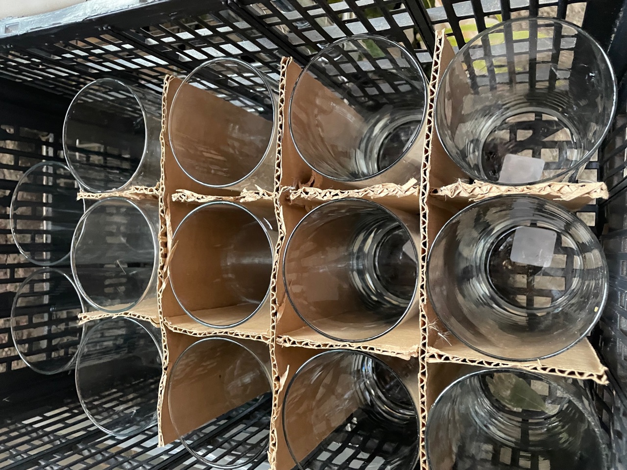 Twelve glass cylinder vases packed upright in a black crate with cardboard dividers between them.