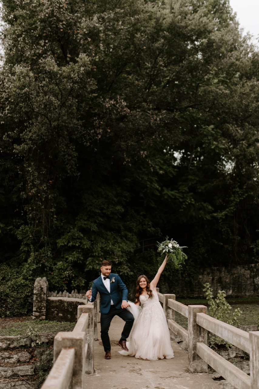 The bride raising her bouquet as the couple cross the stone bridge over Sager Creek.