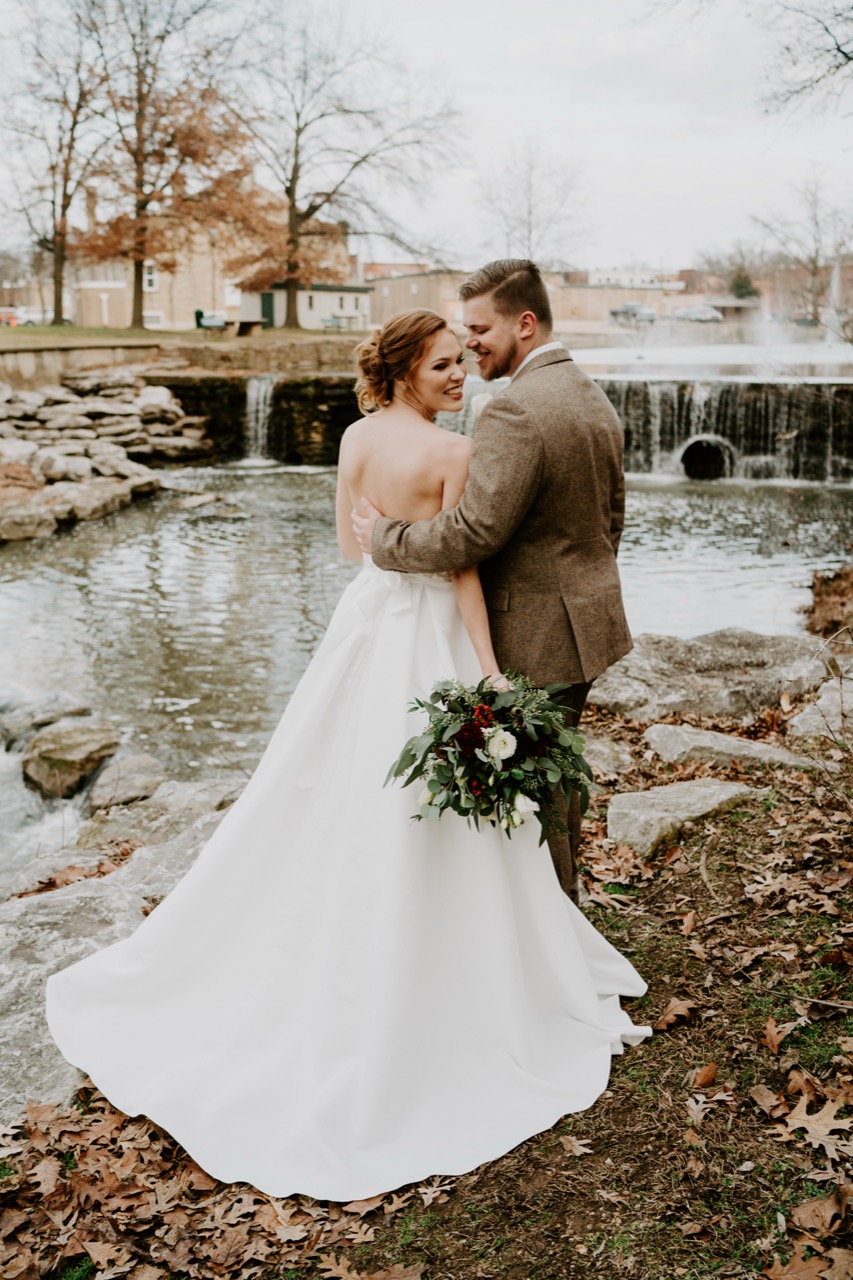 A couple beside the falls on Sager Creek, bare trees and downtown rooftops beyond.