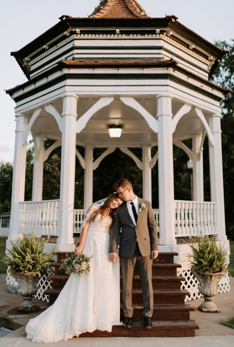 A couple on the steps of the white Victorian gazebo in the park, one block from the ballroom.