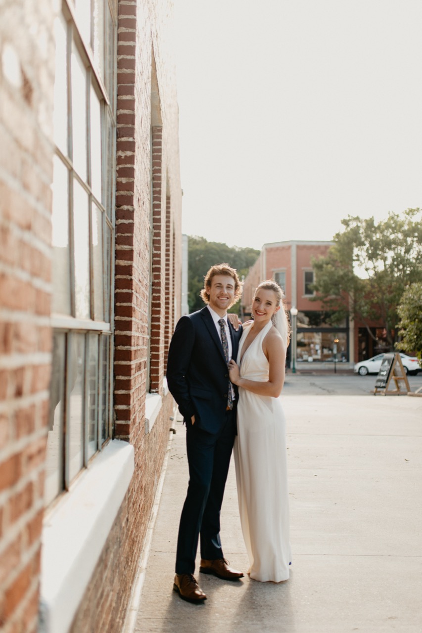 A couple leaning against a brick storefront downtown, late golden-hour light running down the sidewalk.